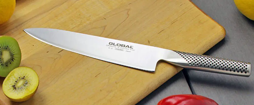 a chef's knife on a cutting board along with some vegetables