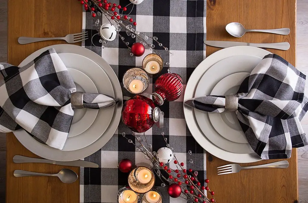 Festive table setting with a farmhouse-style checkered theme, featuring two plates and candles, adorned with red and silver holiday decorations.