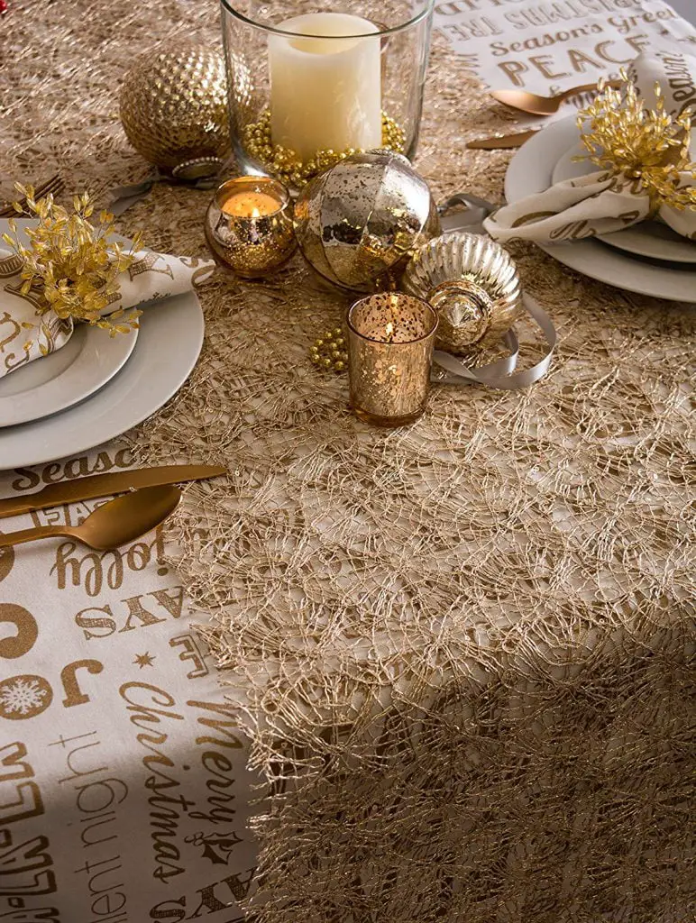 Elegant Christmas table setting with gold decorations, candles, and plates on a shimmering golden tablecloth with festive inscriptions, incorporating Thanksgiving & Christmas farmhouse-style table runners.