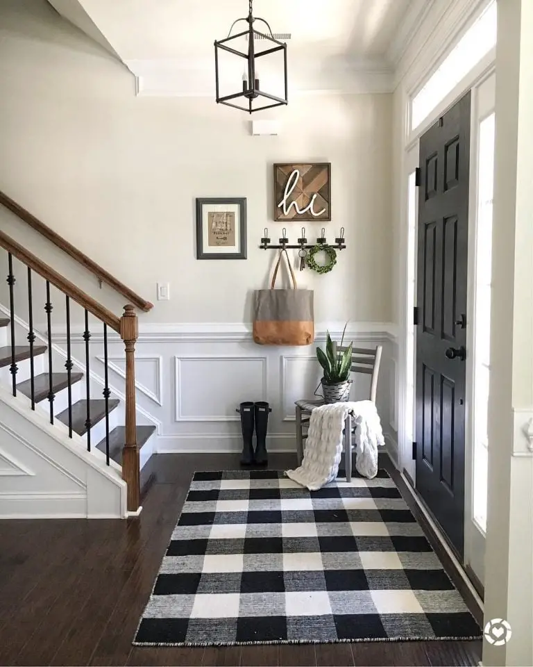 An elegant entryway featuring a buffalo check black and white rug, a wooden staircase, and a modern chandelier, with stylish decor on the walls.