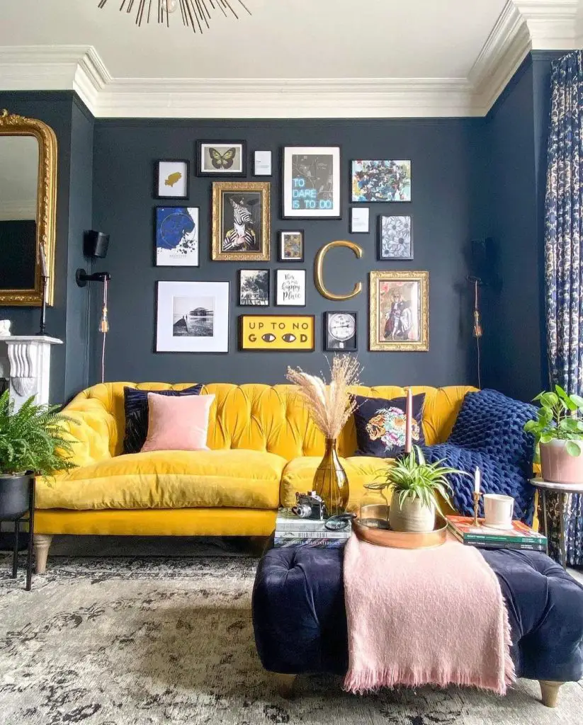 A Guide to Decorating Your Home with Bold Colors features a stylish living room with a dark blue wall filled with various framed artworks, showcasing a mustard yellow sofa, a black round ottoman, and scattered houseplants.