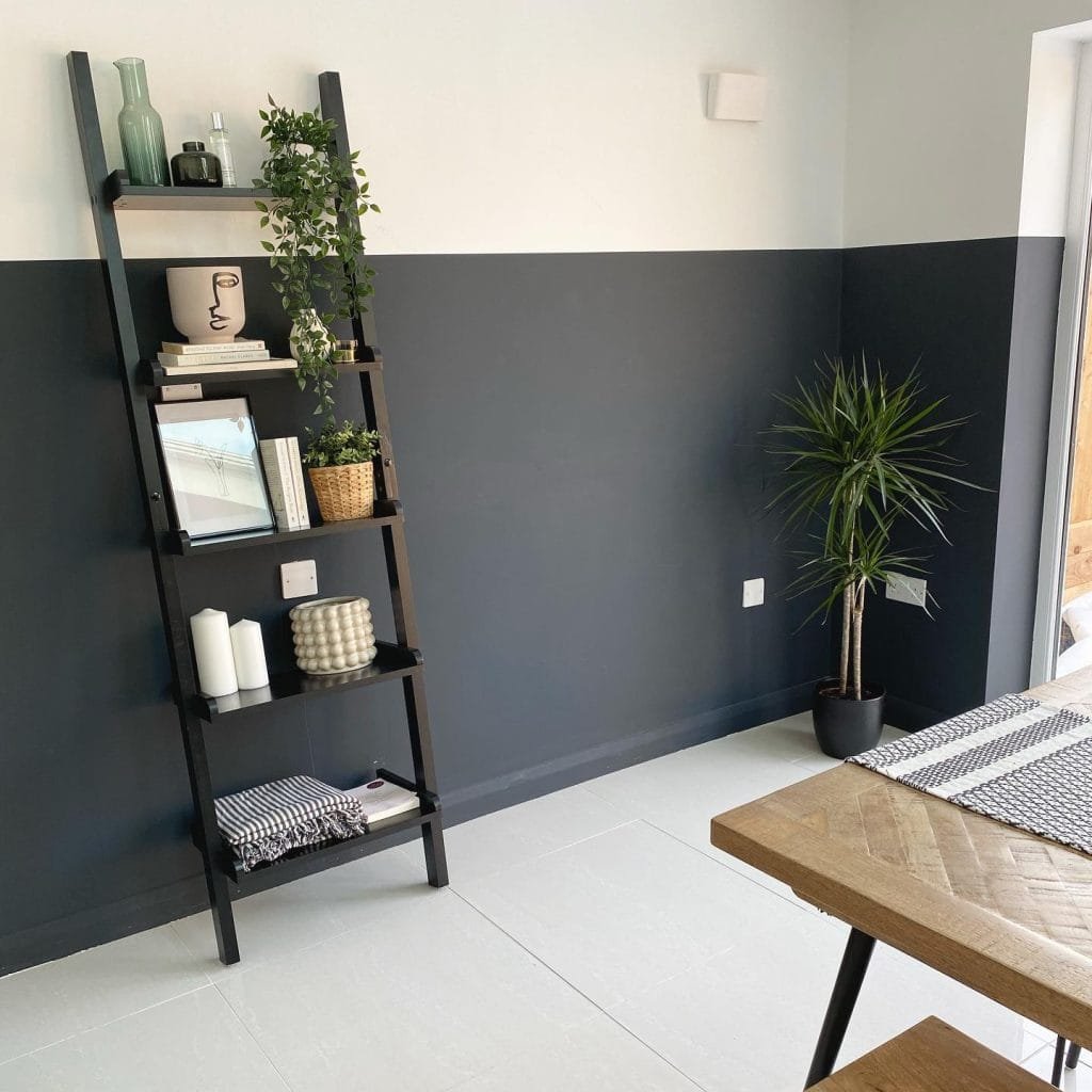 Modern living room corner with dark gray walls, featuring a black ladder shelf with clever storage decor, and a potted plant next to a wood table.