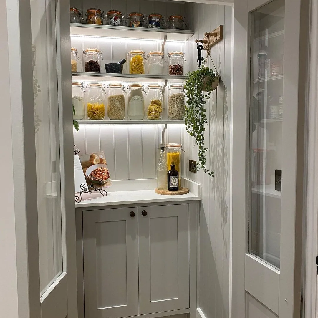 Glass jars and clear containers on pantry shelves in a small white pantry.