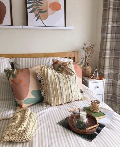 A cozy bedroom corner featuring a bed with stylish pillows, a serving tray with a teacup, art on the wall, and a small wooden side table styled with top summer oasis decor items.