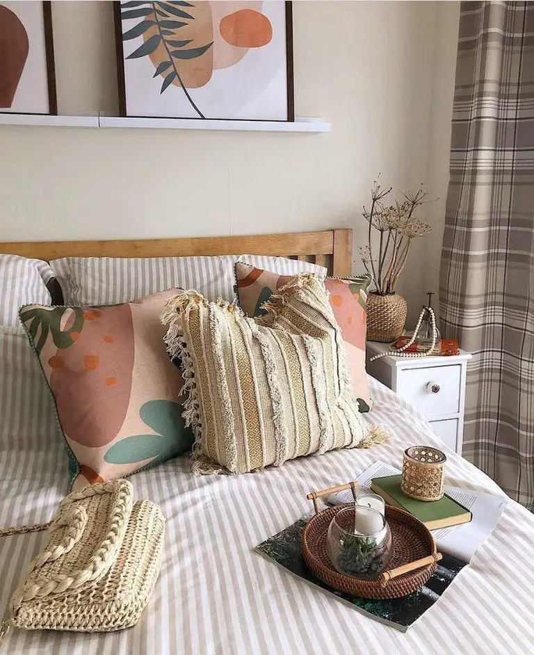 A cozy bedroom corner featuring a bed with stylish pillows, a serving tray with a teacup, art on the wall, and a small wooden side table styled with top summer oasis decor items.