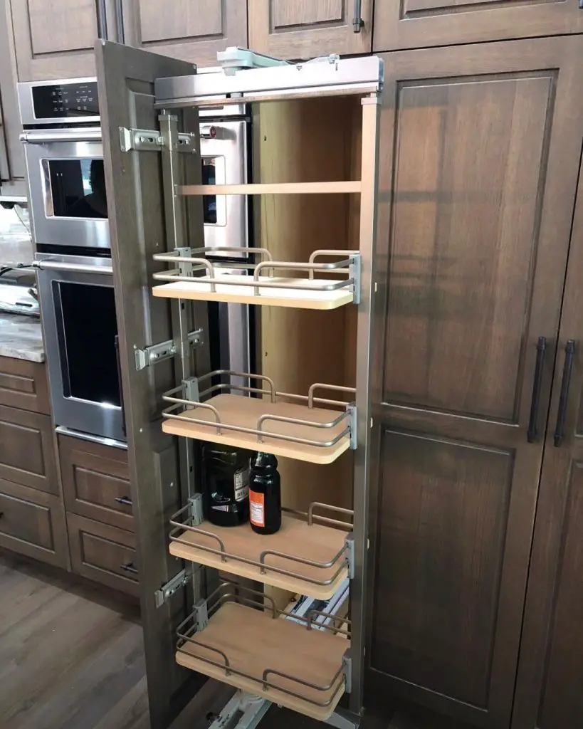 A tall kitchen cabinet with open pull-out shelves, featuring 10 creative ways to optimize your kitchen cabinet space, containing jars and bottles, surrounded by other wooden cabinets and appliances.