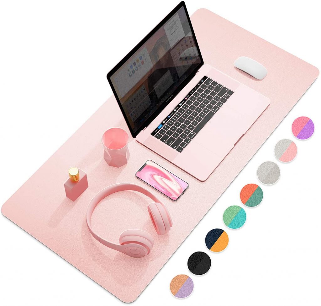 A productive pink-themed workspace featuring a laptop, headphones, mouse, and various accessories on a pink mat, with color swatches nearby.