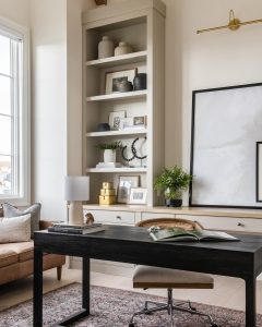 A stylish home office designed to optimize your workspace for maximum efficiency, featuring a black desk with a lamp and books, flanked by a cream sofa, built-in shelving with decor, and a large abstract art piece.