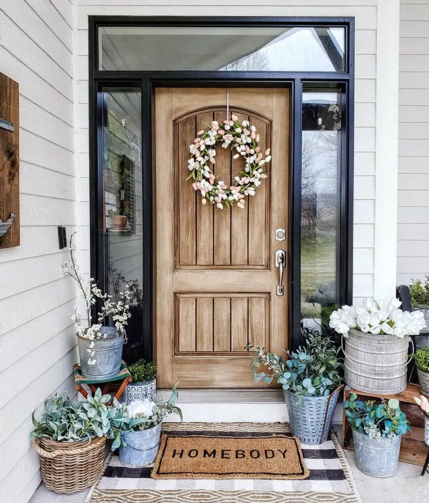 Winter front porch decor with a beautiful door wreath and potted flowers on the floor next to layered door mats