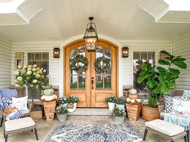 a double-door fall front porch with seatings and potted plants on the floor including some pumpkins
