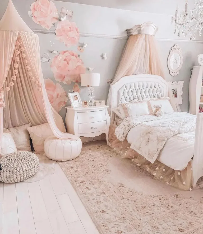 A cozy bedroom with a white and pink color scheme, featuring a bed with a tufted headboard, a canopy, a nightstand, and floral wall decorations. A play tent and plush seating are in the corner—one of 17 pink bedrooms fit for a princess.