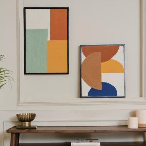 Two abstract paintings with geometric shapes hanging over a wooden console table, alongside decorative wall art items, in a room with a neutral color scheme.
