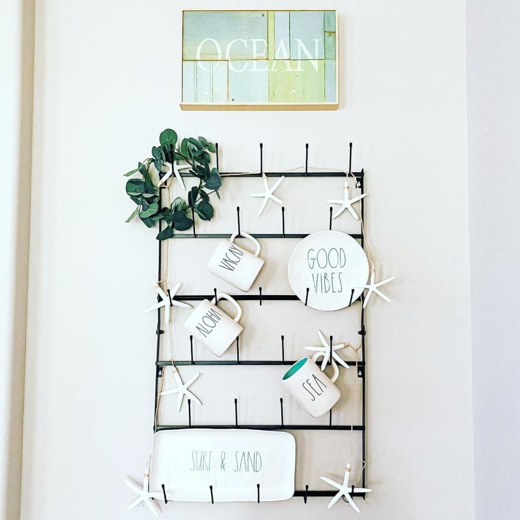 A coastal-inspired wall display featuring a grid with decorative starfish and plaques labeled "Aloha," "Good Vibes," "Sun," and "Surf & Sand," topped with an "OCEAN" sign.