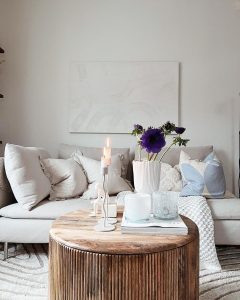 A cozy living room with a plush sofa, round wooden coffee table adorned with candles, books, and flowers, and a large abstract art piece on the wall incorporating elements of Scandinavian design.