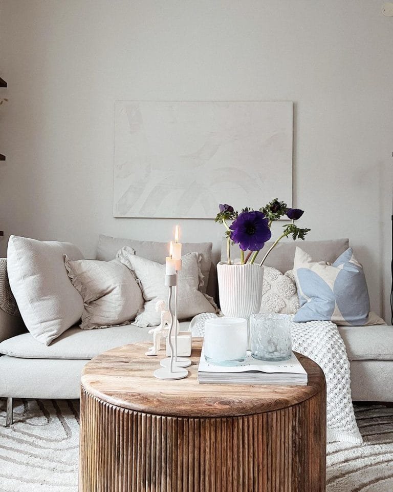 A cozy living room with a plush sofa, round wooden coffee table adorned with candles, books, and flowers, and a large abstract art piece on the wall incorporating elements of Scandinavian design.