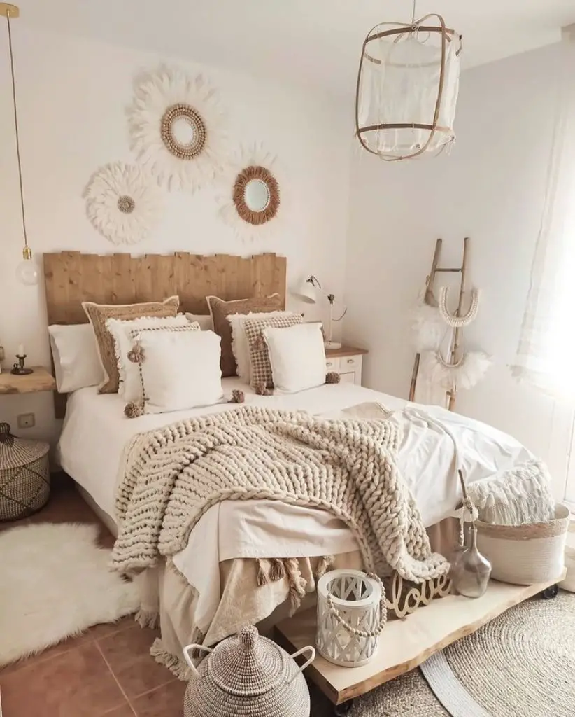 A cozy bedroom featuring a neutral color scheme with a wooden headboard, white bedding, chunky Boho-chic throw blanket, hanging light, and decorative woven items.