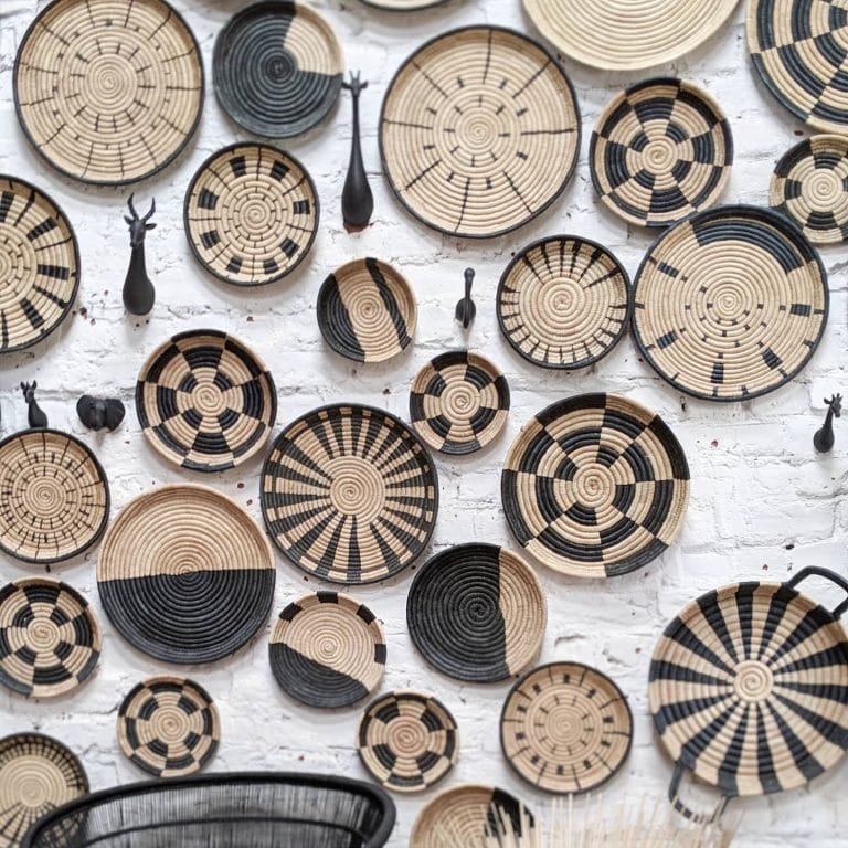 A collection of black and beige Bohemian woven baskets and African decorative items displayed on a white wall.