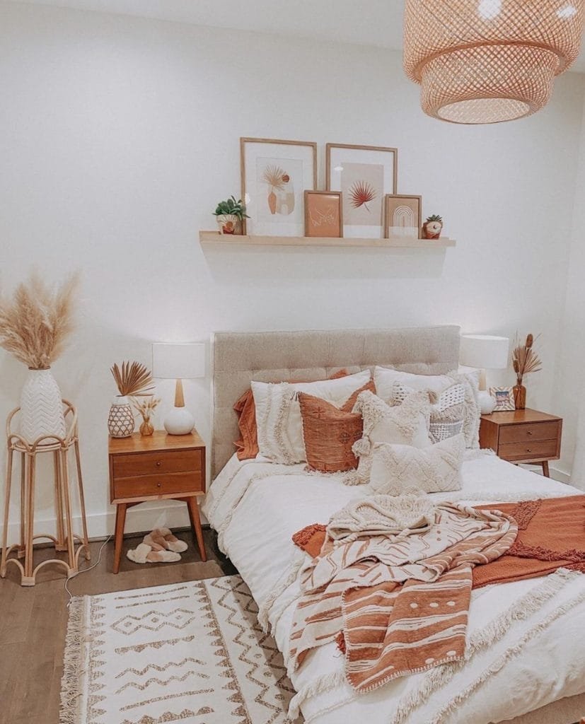 Cozy bedroom with a neatly made bed, Boho-chic rug, floating shelf with art, and warm lighting. Decor includes earth-toned linens and decorative plants.