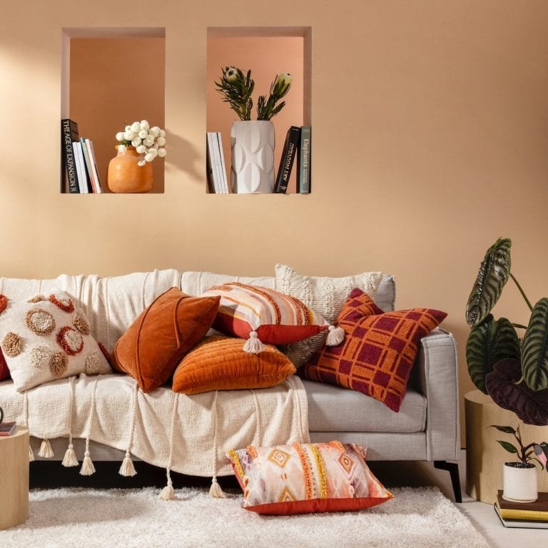 Cozy living room with a gray sofa adorned with Bohemian throw pillows, two wall-mounted shelves holding books and vases, and a plush white rug on the floor.