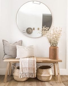 A minimalist entryway with a bench, round mirror, decorative pillows, and baskets under a wooden bench. Neutral tones and 10 ways to make your entryway bench look more inviting add warmth.

