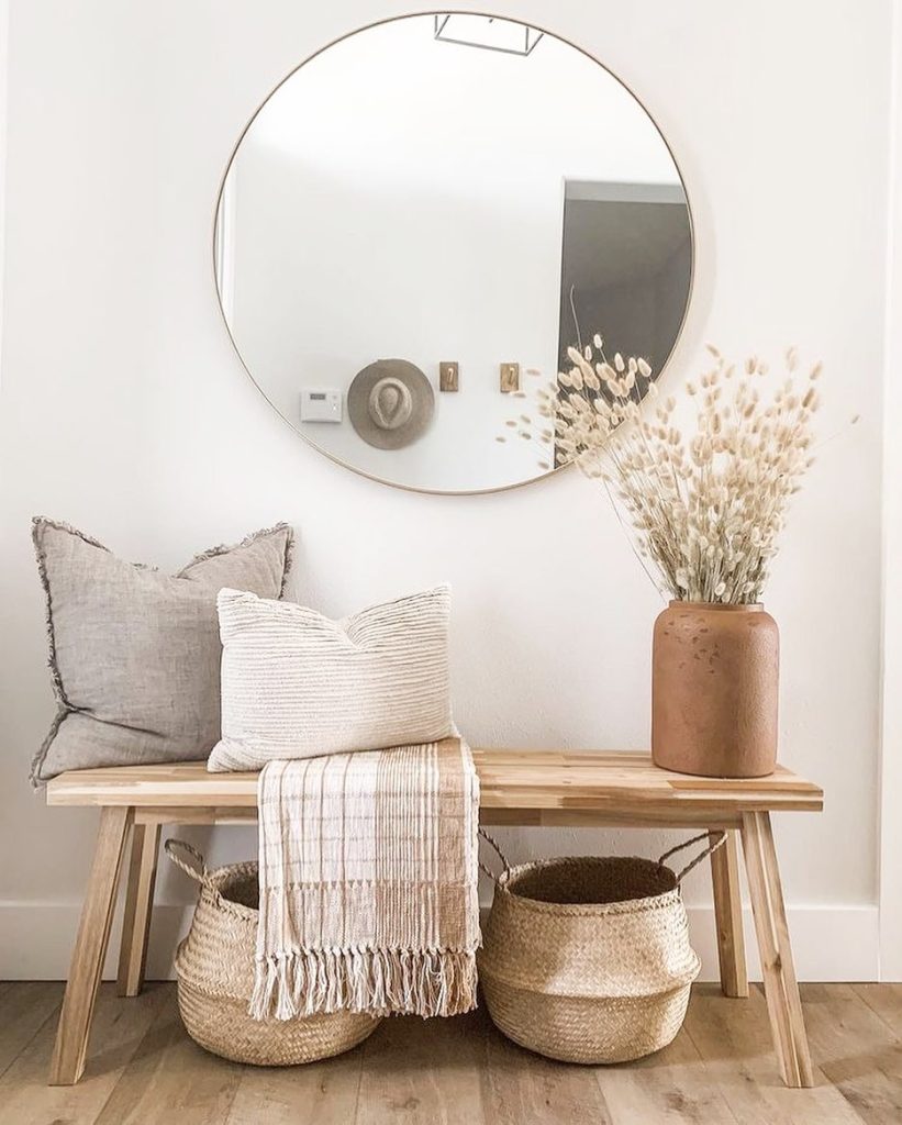 A minimalist entryway with a bench, round mirror, decorative pillows, and baskets under a wooden bench. Neutral tones and 10 ways to make your entryway bench look more inviting add warmth.