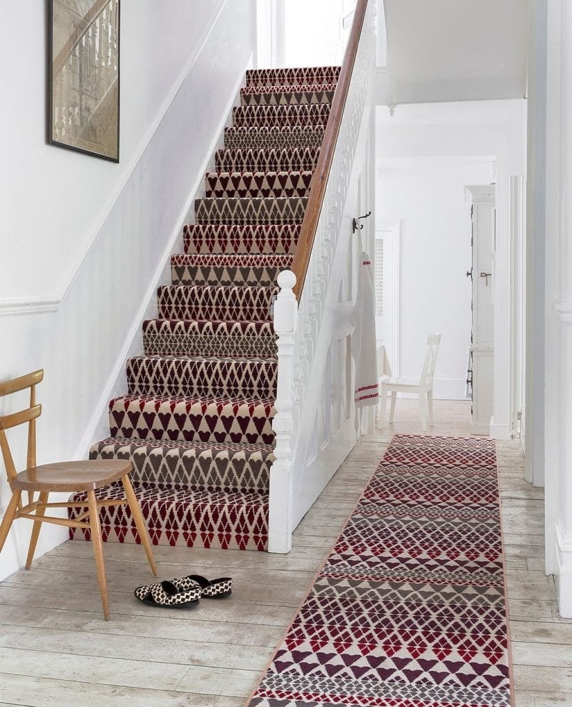 A hallway featuring a white staircase with a patterned red and white runner, a matching hallway rug, and a wooden chair