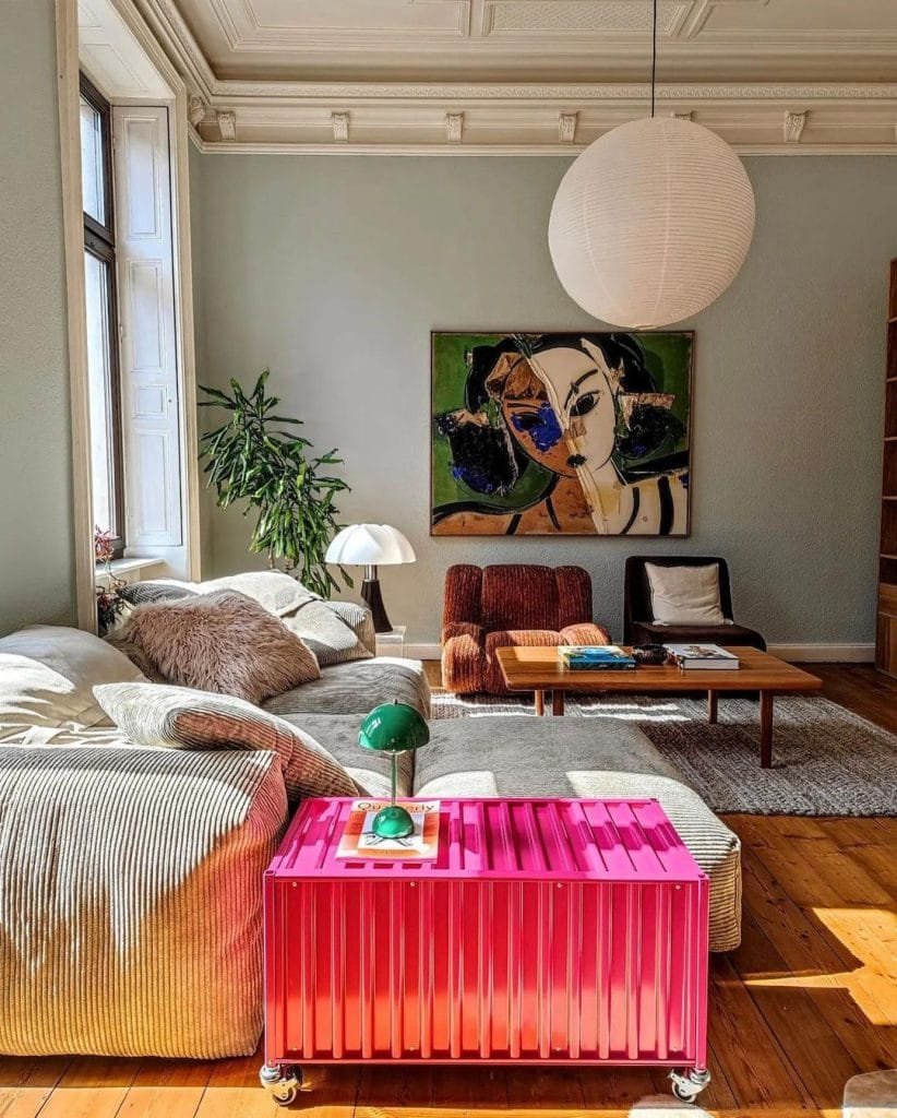 Bright living room with a large modern painting, a pink ribbed coffee table, and a white sofa surrounded by assorted plants and funky lamps.