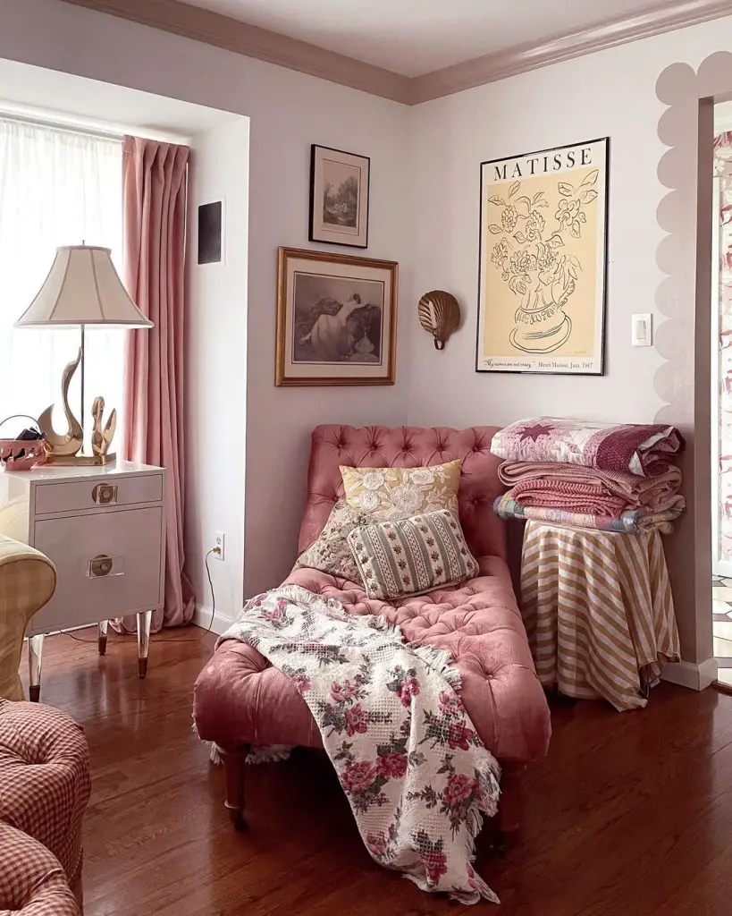 A cozy living room corner featuring a pink chaise longue adorned with a floral blanket, a white side table with a lamp, and a vintage Matisse poster on the wall.