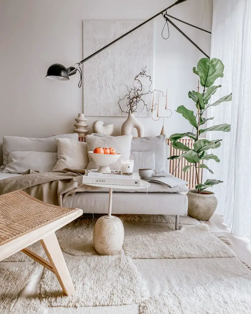 A cozy living room corner featuring a gray sofa with orange accents, a large floor lamp, white abstract painting, and a vibrant potted plant beside a Scandinavian wicker chair.