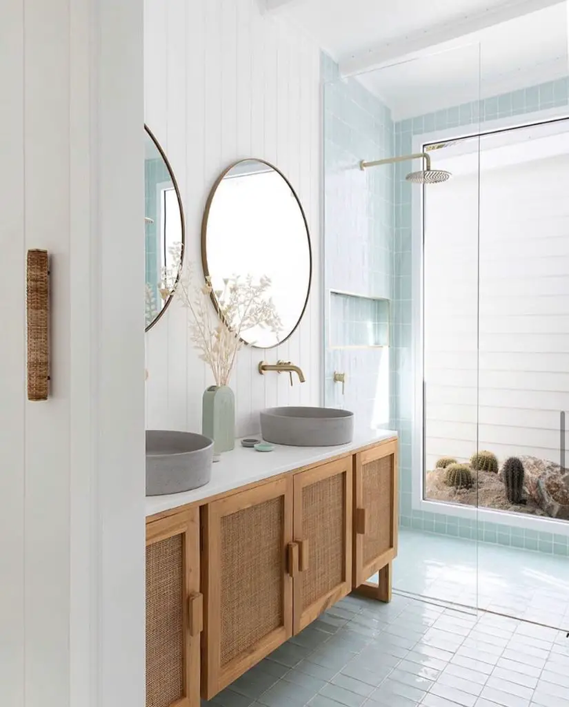 Modern Coastal Boho bathroom featuring double vanity with oval mirrors, wooden cabinetry, teal tiles, and a glass shower area.
