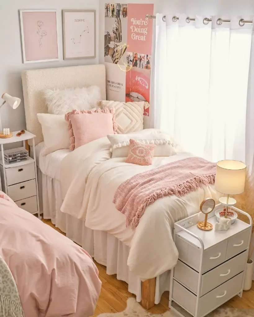 A cozy, well-decorated bedroom with a plush bed covered in pink and white bedding, inspirational wall art, and soft lighting from a bedside lamp. Discover 5 unique ways to personalize your dorm room decor while maintaining this charming aesthetic.