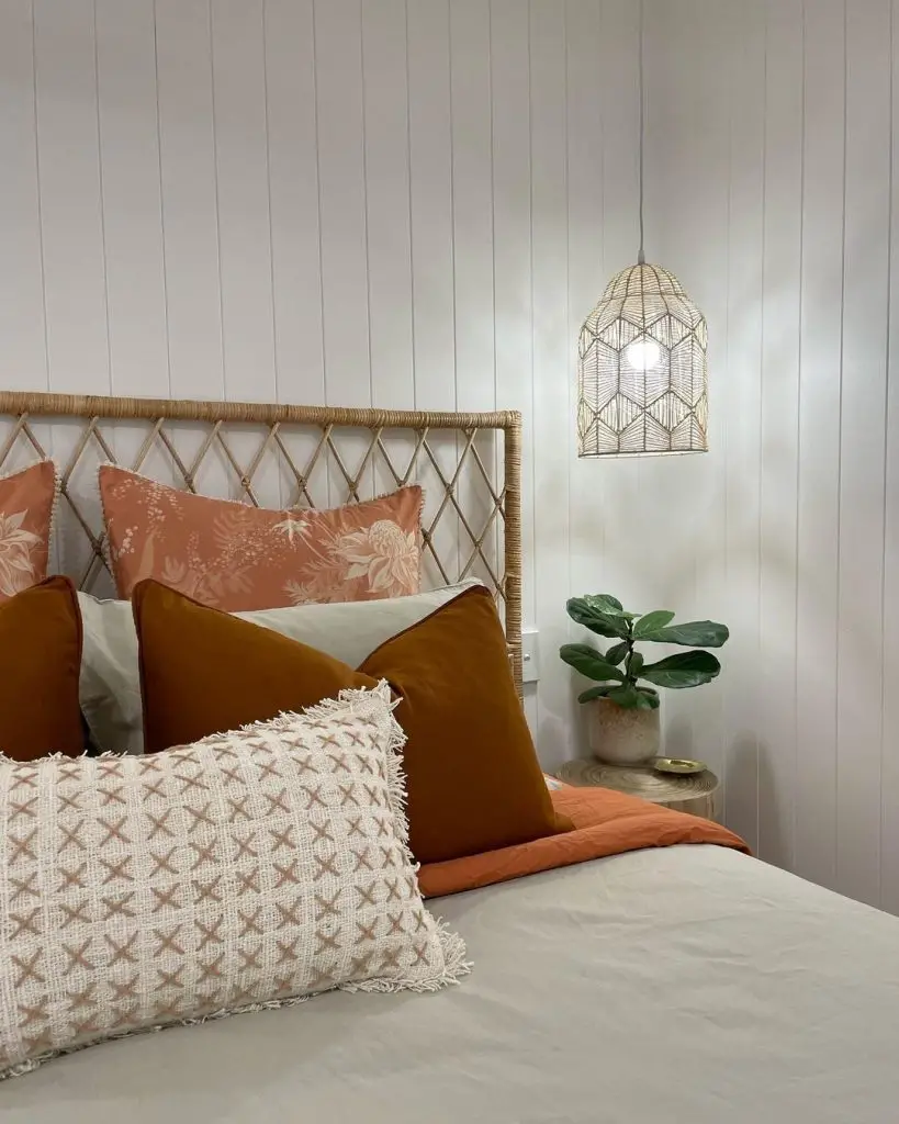 A cozy bedroom corner featuring a rattan headboard with decorative pillows, an eclectic hanging lantern light, and a potted plant beside the bed.