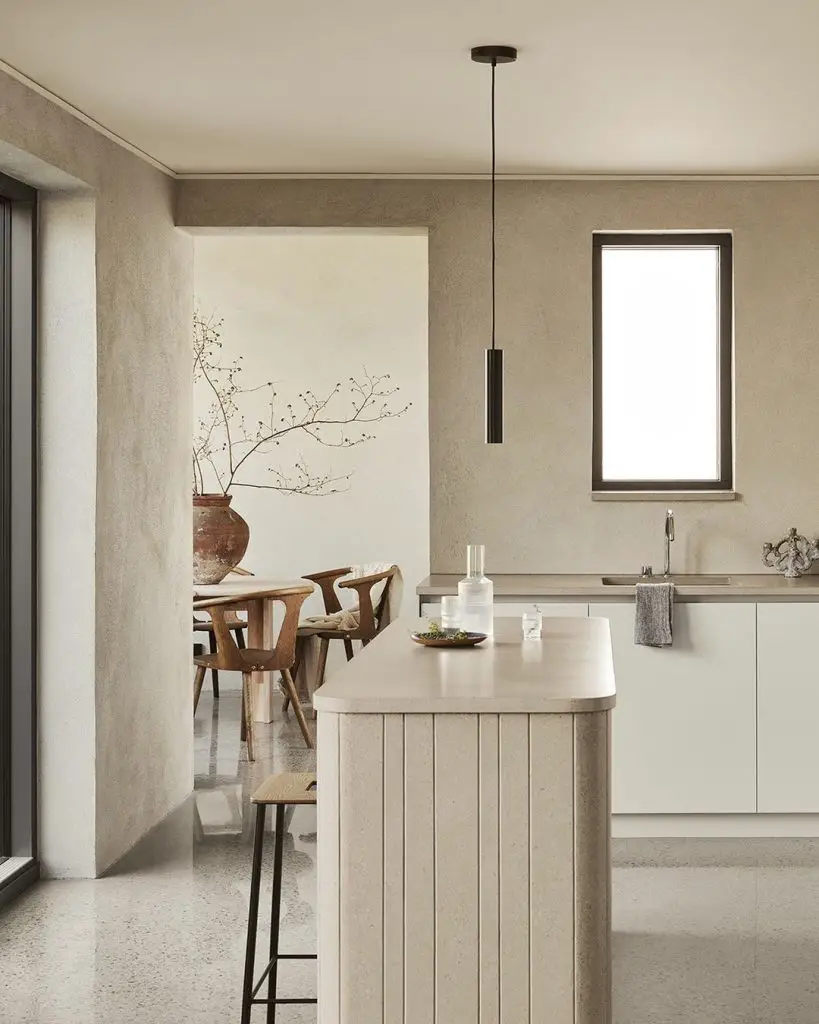 Modern kitchen with a central island, pendant light, minimalist wooden furniture, and large windows. Neutral tones and natural light create a serene ambiance. Learn how to design a minimalist kitchen that's both functional and beautiful.