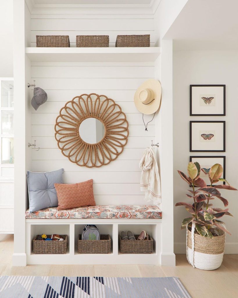 A cozy entryway nook with a mini bench, storage baskets, a decorative round mirror, hanging hats, and framed butterfly prints on the wall.