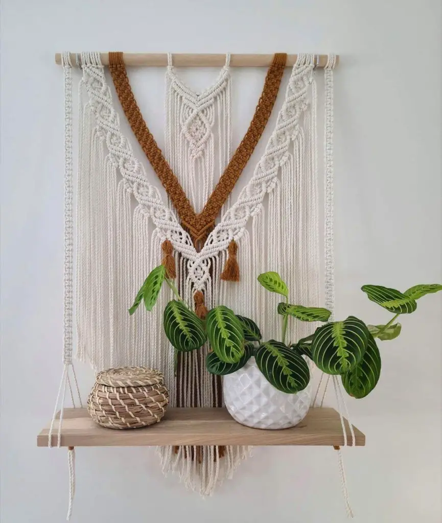 A wooden shelf holds a potted plant with green leaves and a woven basket. Behind it, showcasing how to style bohemian charm from hippie to chic, hangs a macramé wall hanging with white and brown yarn.