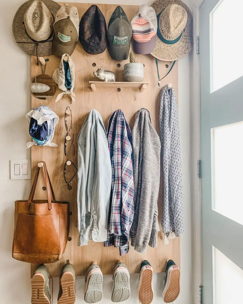 Organization Made Stylish: Wooden wall organizer with six hats, five pairs of shoes, three jackets, a bag, a cloth, glasses, a small plant, and other small items near a door with frosted glass panels.
