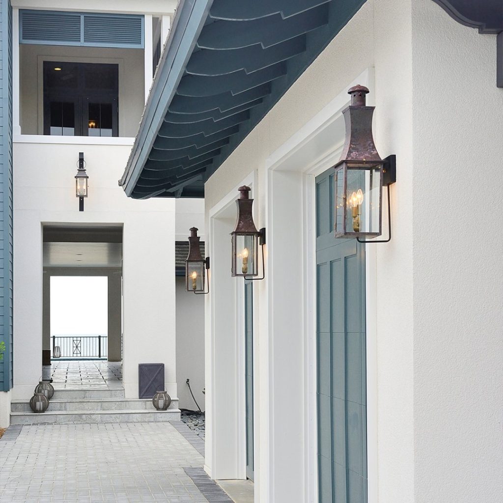 Exterior view of a modern house with blue trim and white walls, featuring multiple lantern-style wall lights—an excellent example from "7 Creative Ways to Use Wall Sconces in Your Coastal Decor"—and a pathway leading to an open balcony with a distant water view.