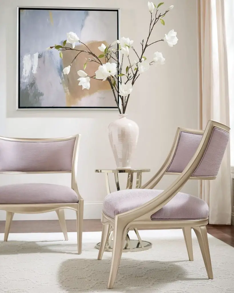 A contemporary living room features two light pink chairs, a white vase with white flowers on a small table, and abstract wall art. For tips on creating this look, see "Living Room Decor: How to Choose the Best Accent Chair.