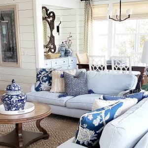 A cozy living room with blue and white floral decor exuding Southern Decor Elegance: 10 Essential Elements for a Sophisticated Home. There are two sofas, a round coffee table, and a dining area in the background. Decor includes patterned cushions and a decorative urn.