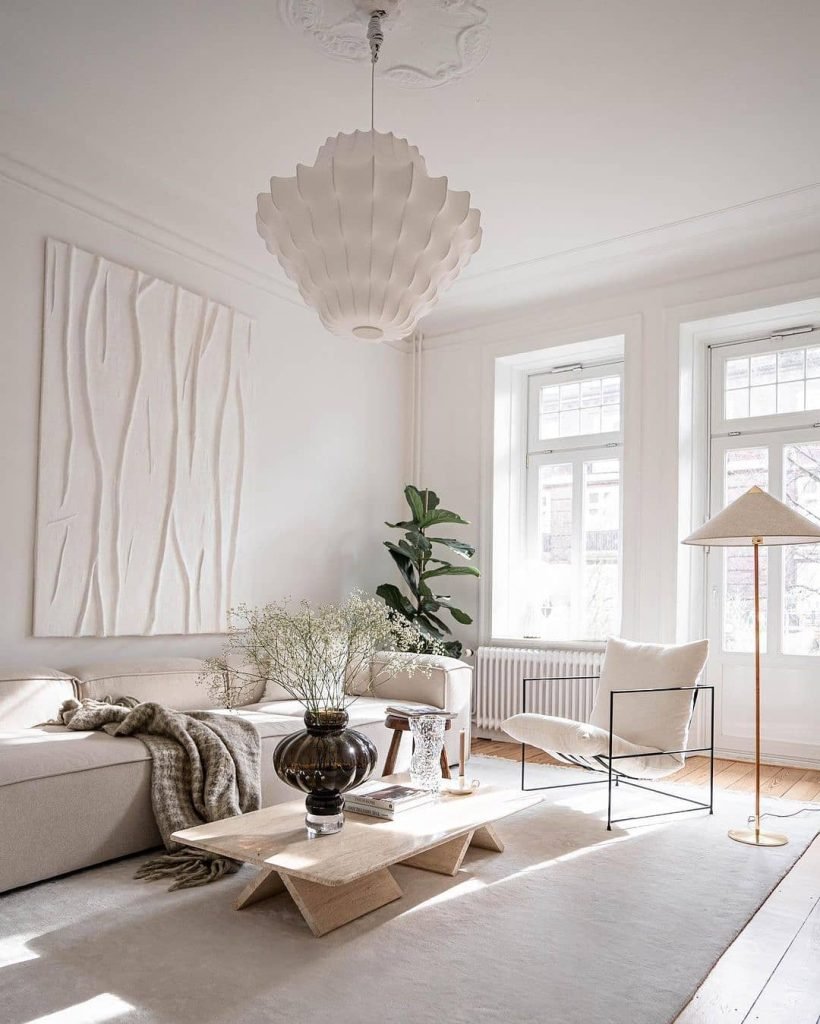A bright, minimalist living room with white walls, a white couch, a wooden coffee table, and a tall plant. Natural light streams through large windows while the cream armchair's perfect positioning highlights Living Room Decor: How to Choose the Best Accent Chair ideas.