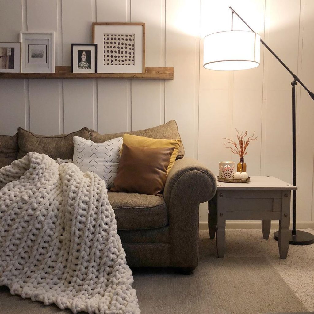 warm interior living space couch and floor lamp with a wood panel wall and a floating shelf in the background
