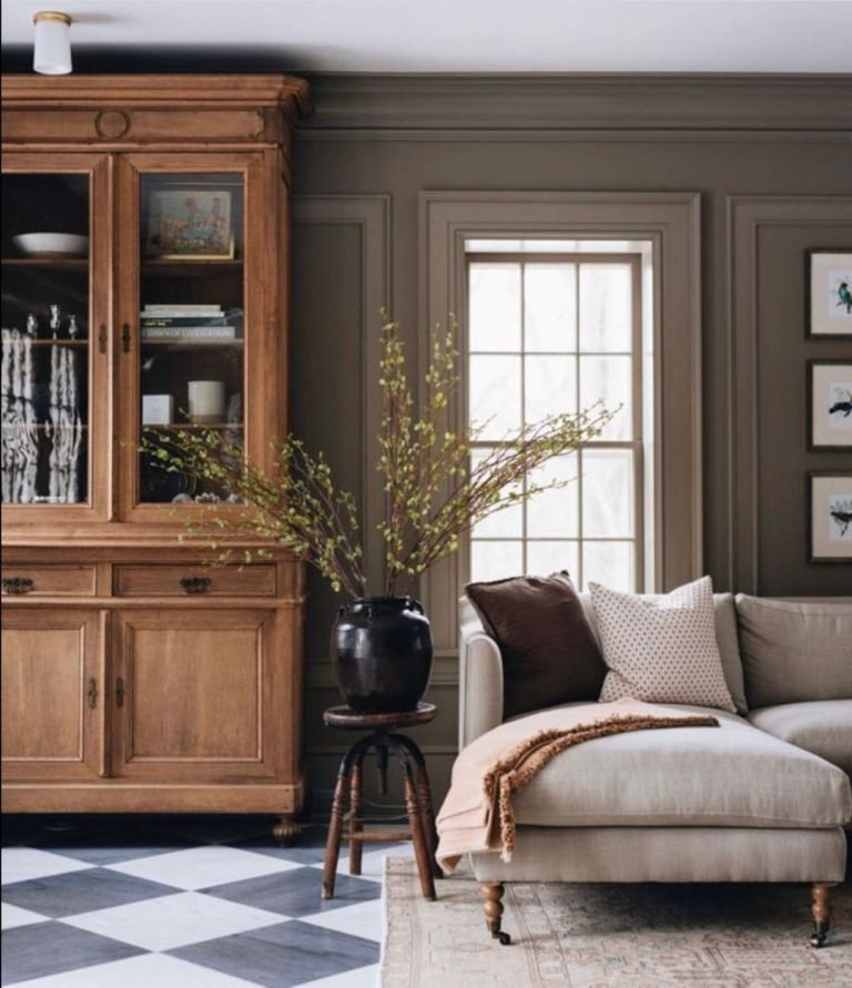 modern rustic interior living space with a throw pillow style couch, potted flower on an end table, a wooden wall cabinet with glass doors, and a window in the background