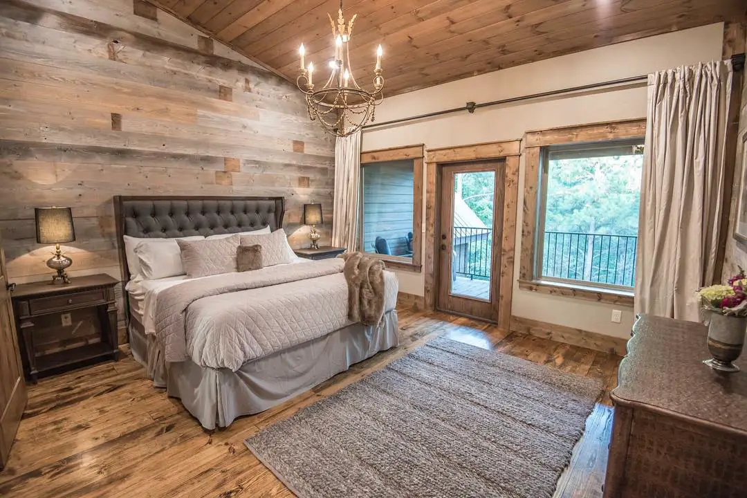 rustic looking bedroom with wood flooring and ceiling and a tufted upholstered bed styled with a candle lamp ceiling chandelier