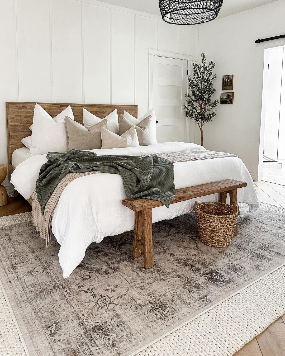 a wooden headboard bed and matching end wooden bench styled on a patterned floor rug in a white painted modern rustic bedroom