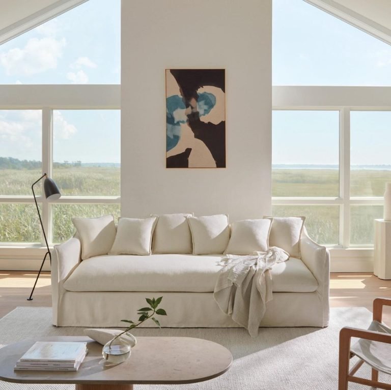 all white living space interior with a long slipcover sofa, floor lamp, and a coffee table