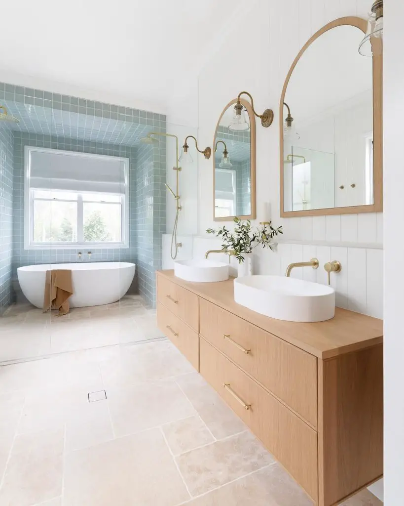 a coastal-style bathroom interior with a wooden double vanity, wall mirrors, and a white freestanding bathtub