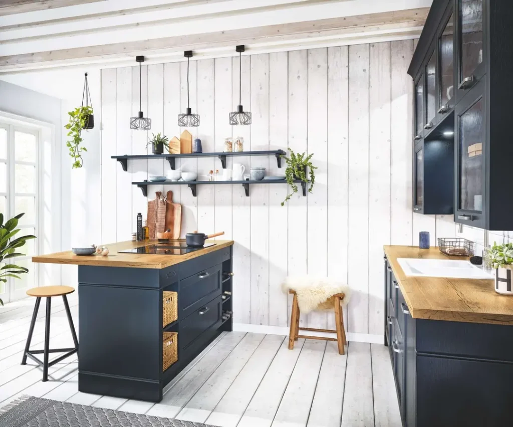 Modern kitchen with dark cabinets, wooden countertops, and hanging pendant lights. Features a central island with stools, open shelving, and potted plants against a white shiplap wall—a perfect blend to achieve the modern coastal kitchen look.