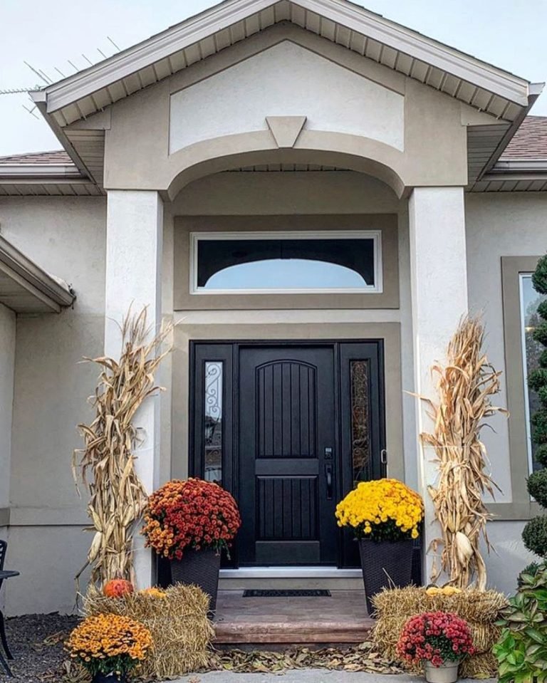 outdoor entry porch of a home with a fibreglass door paired with wrought iron glass, and potted plants on both sides of the covered entryway