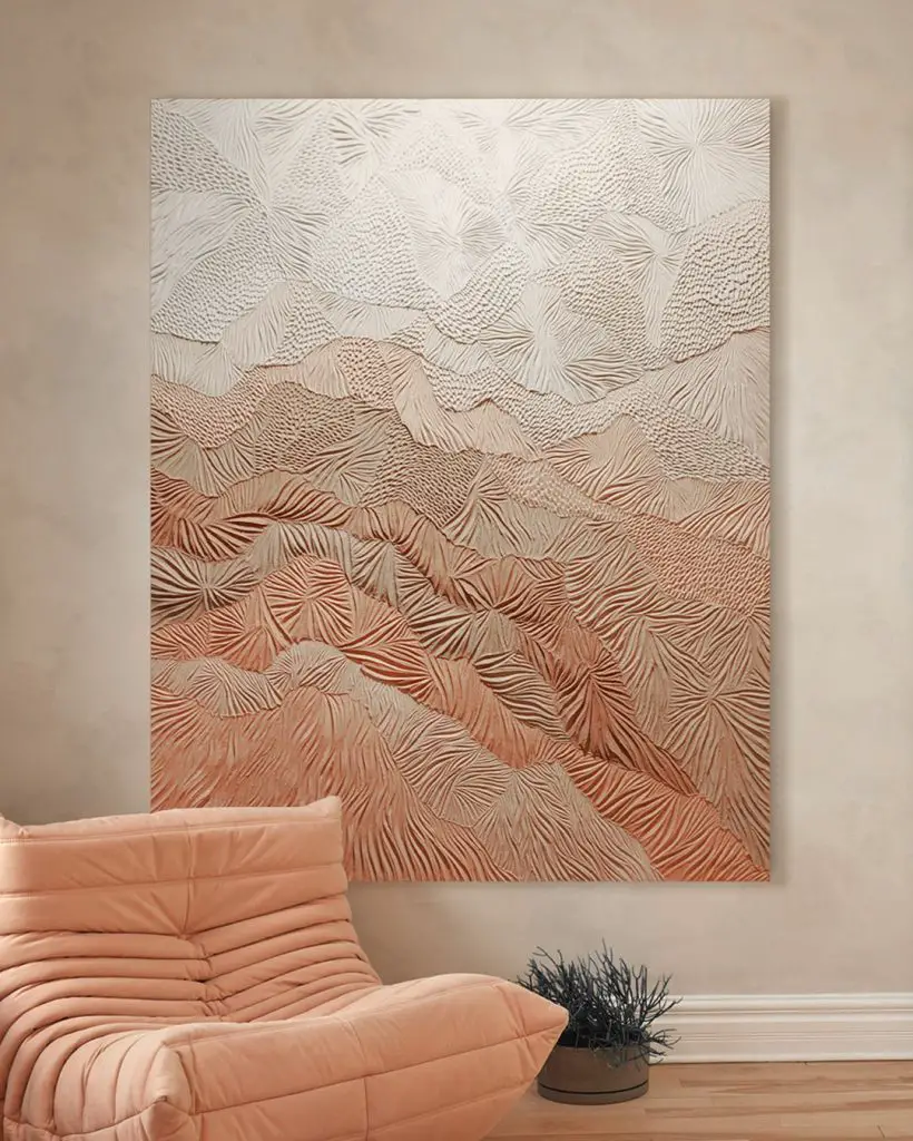 How can you embrace creative ideas beyond paint and wallpaper? Consider a textured abstract wall art with a landscape pattern in earthy tones, hanging on a beige wall above a peach-colored cushioned chair and a small plant.
