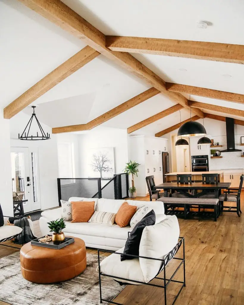 an open plan living and kitchen space, some white seatings in the living space all covered by a double pitch ceiling with exposed wood beams